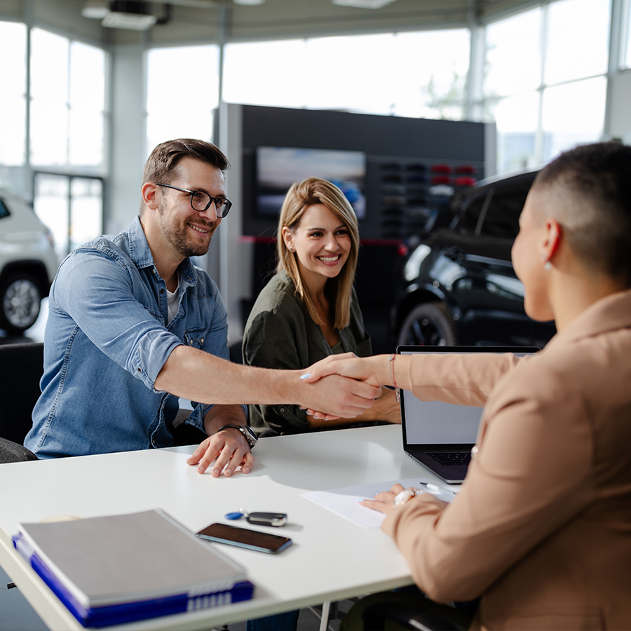 Male customer and female car dealer shaking hands at showroom.