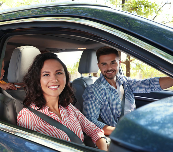 Two people smiling in the front of a vehicle