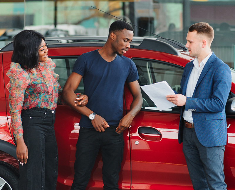 Couple smiling at salesman with a red car.
