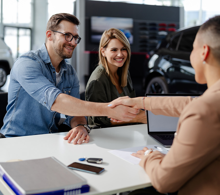 Shaking hands above car paperwork and keys