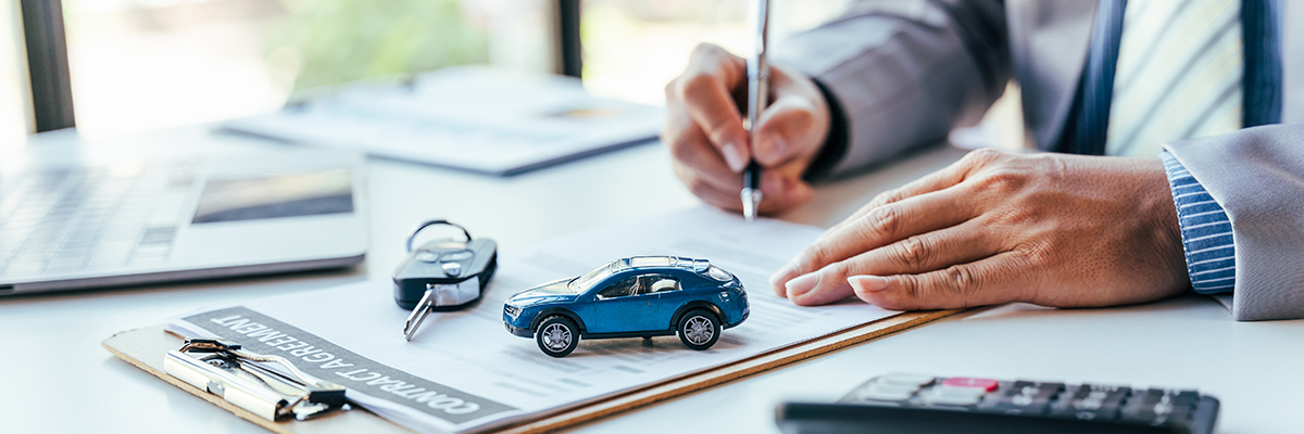 Man signing car insurance document or lease paper. Writing signature on contract or agreement. Buying or selling new or used vehicle. Car keys on table. Warranty or guarantee. Customer or salesman.