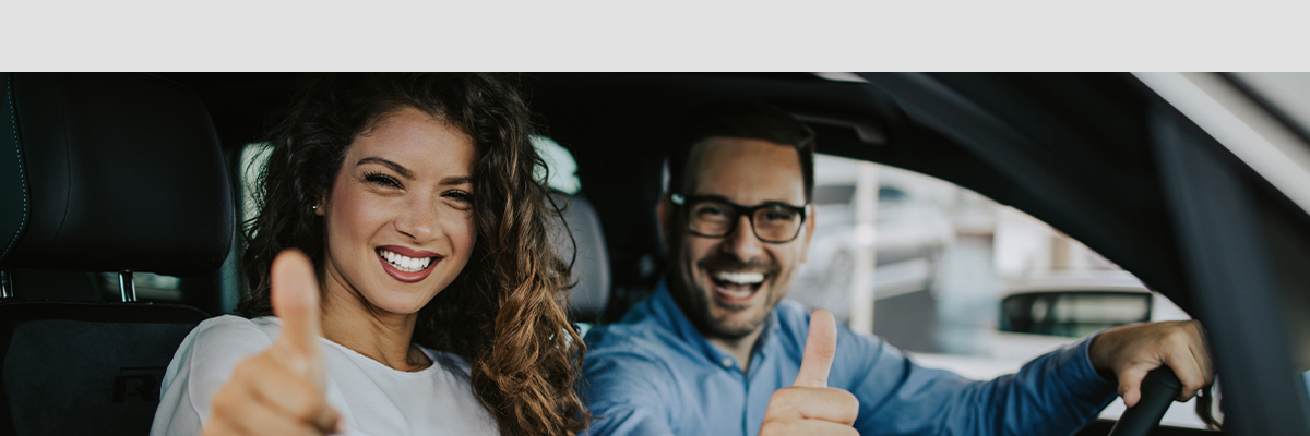 Happy couple in a new car, giving thumbs up
