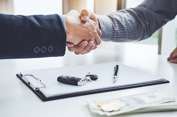 Shaking hands above car paperwork and keys