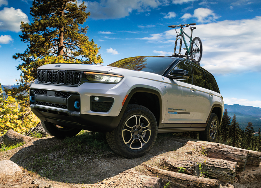 2022 Mopar Grand Cherokee (WL) Trailhawk 4xe in Bright White parked at the top of a rocky trail, with cloudy blue skies overhead and valley, lake, and mountains in the distance.