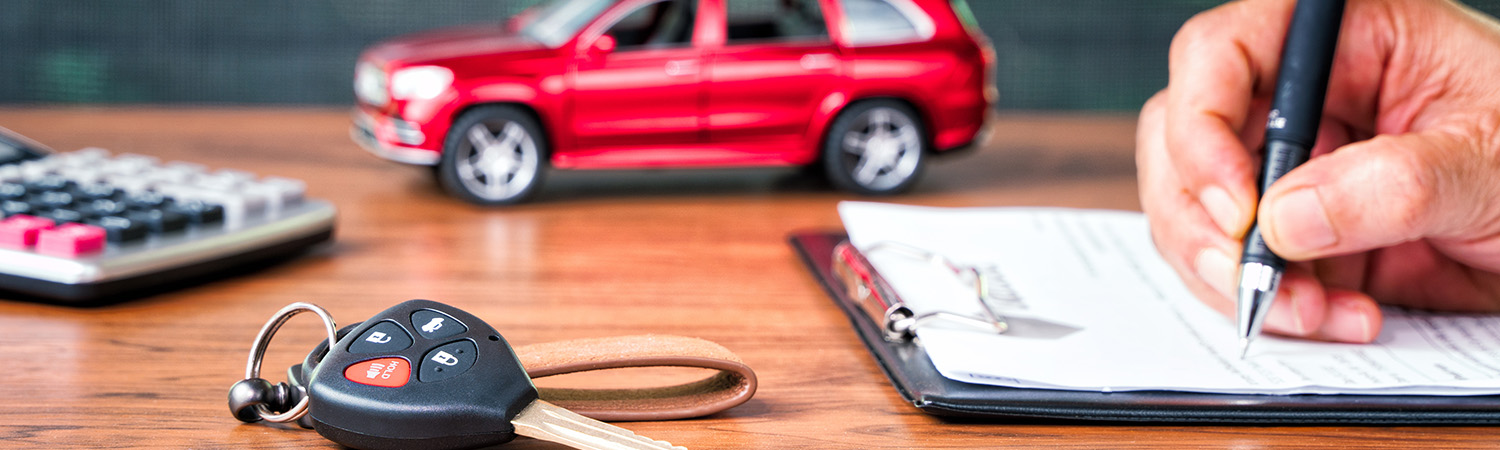 close up of person signing paperwork with car keys on the desk