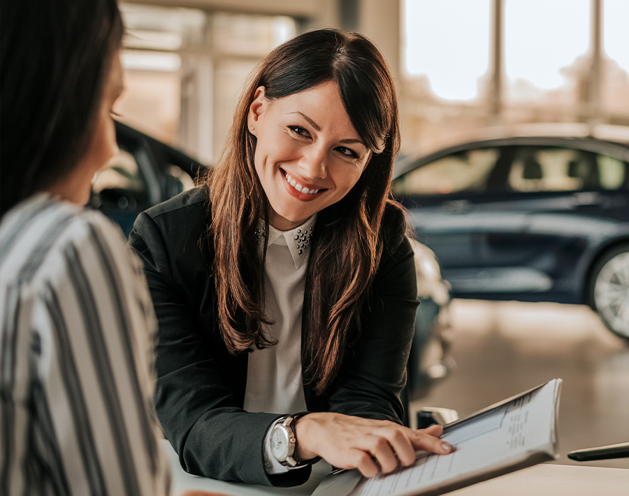 Smiling car saleswoman discussing a contract with a female customer.