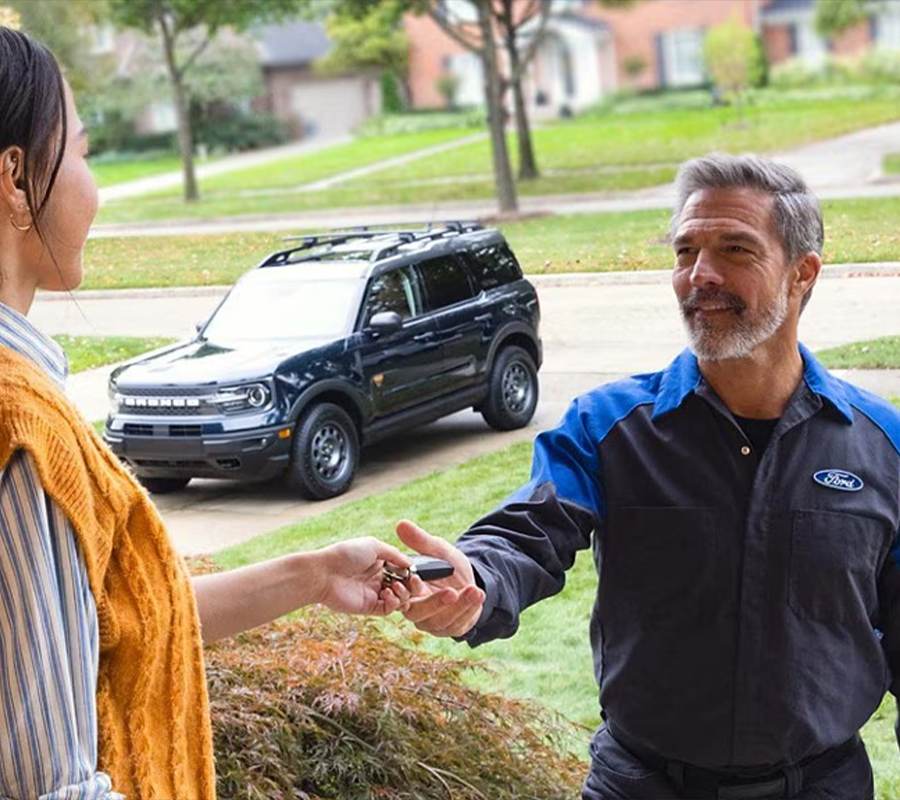 A Ford service tech at a customer’s home is handed their Bronco Sport keys to perform Pickup & Delivery service