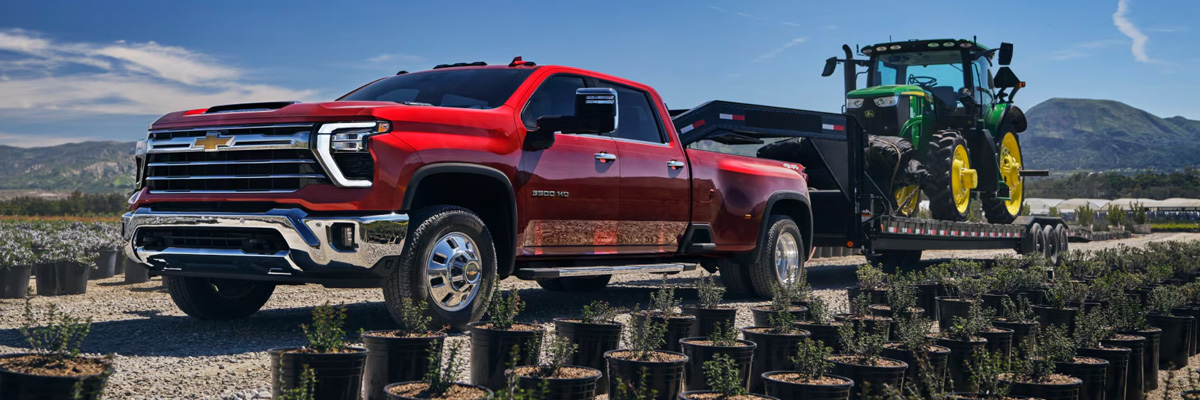 Three Quarters View of a Red 2025 Chevy Silverado HD Towing a Tractor