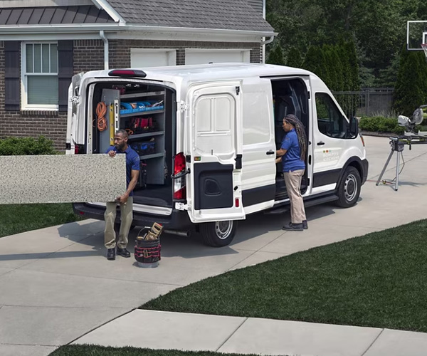 Rear view of a 2025 Ford Transit® Cargo van parked in a driveway with the side and rear cargo doors open