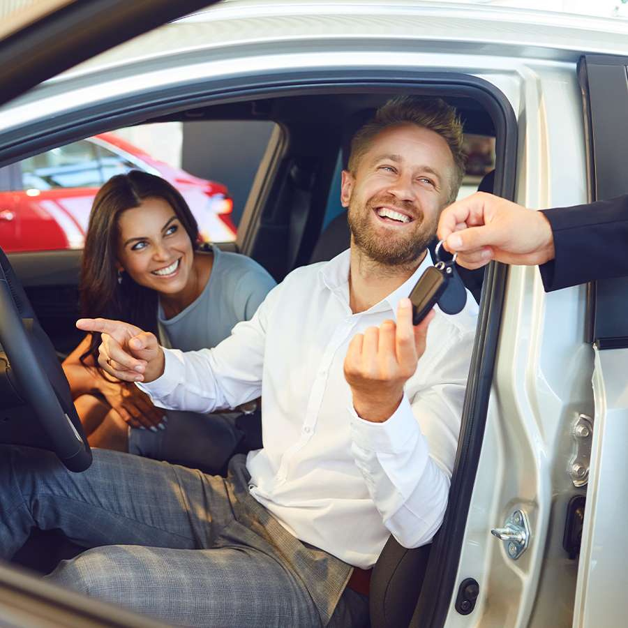 someone handing over car keys to a happy couple in their new car