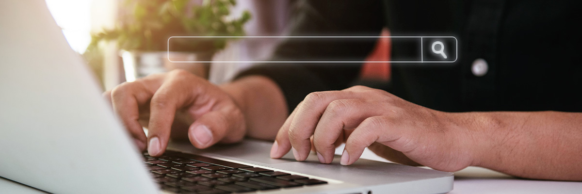 Close up of hands on a laptop keyboard with a search bar overlayed on the image