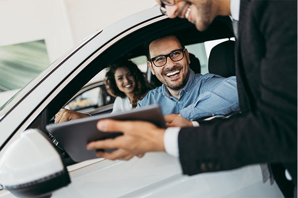 Customers smiling at dealership employee inside of car