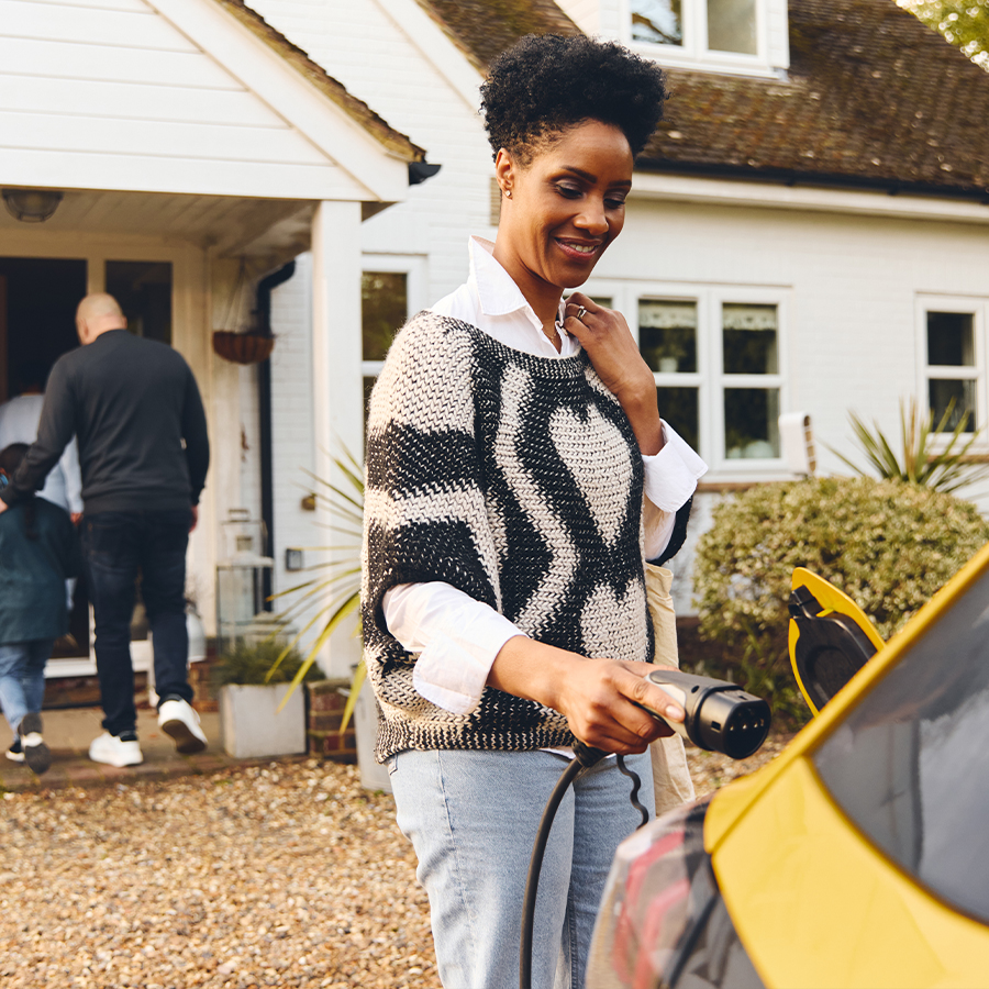 Woman plugging in electric charger into car with family outside home