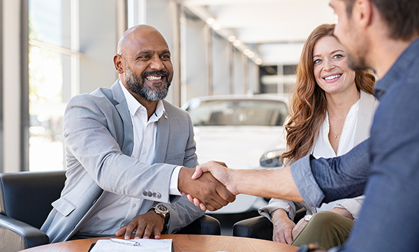 customers at a car dealership, shaking hands with sales person