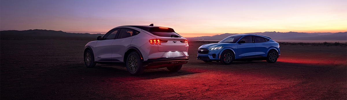  The backside of white Ford Mustang Mach-E® and side view of a blue Ford Mustang Mach-E® at sunset