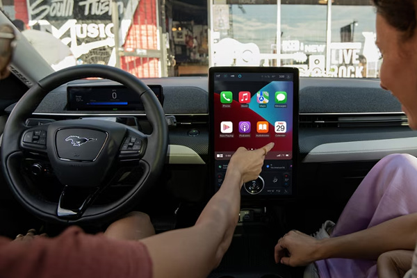 A driver and a passenger are in the front seats of a Ford Mustang Mach-E while using Apple CarPlay