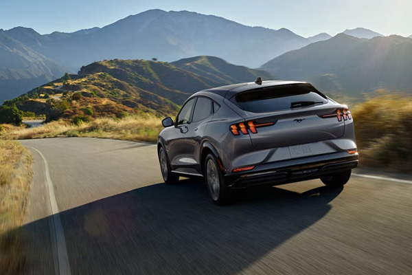 A gray Ford Mustang Mach-E drives along a long, winding road