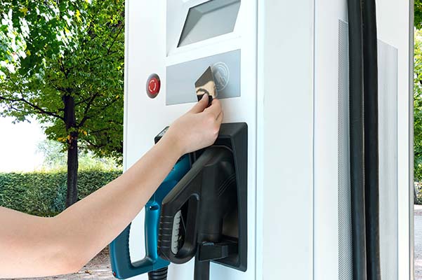 Hand holding pre-paid card to refill money for EV machine at charging station with nature background