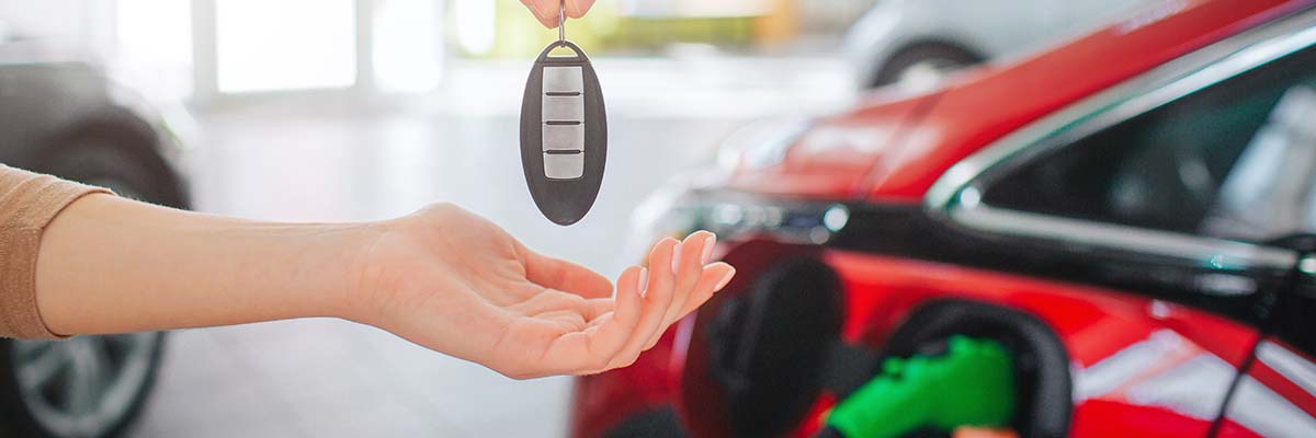 Young family buying first electric car in the showroom. Close-up of male hand giving car key to female hand on battery electric car background