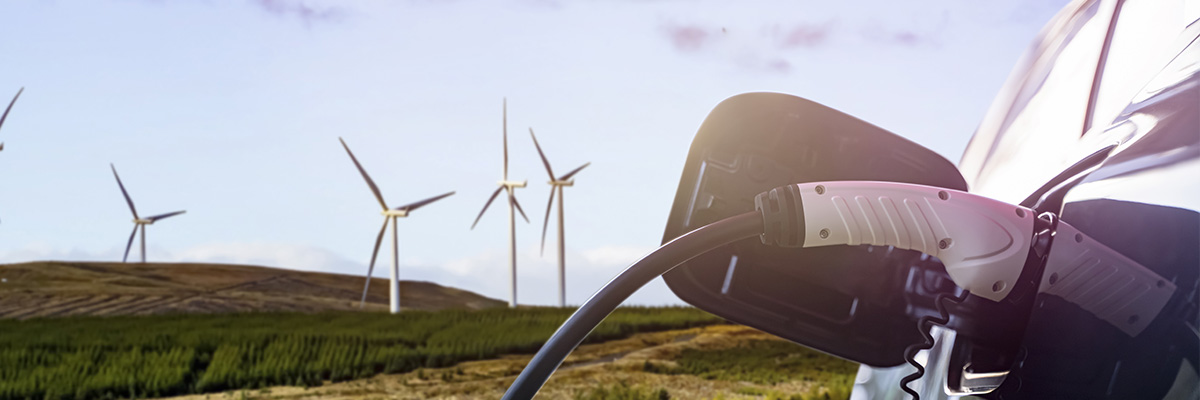 EV car charging at station in front of wind turbines