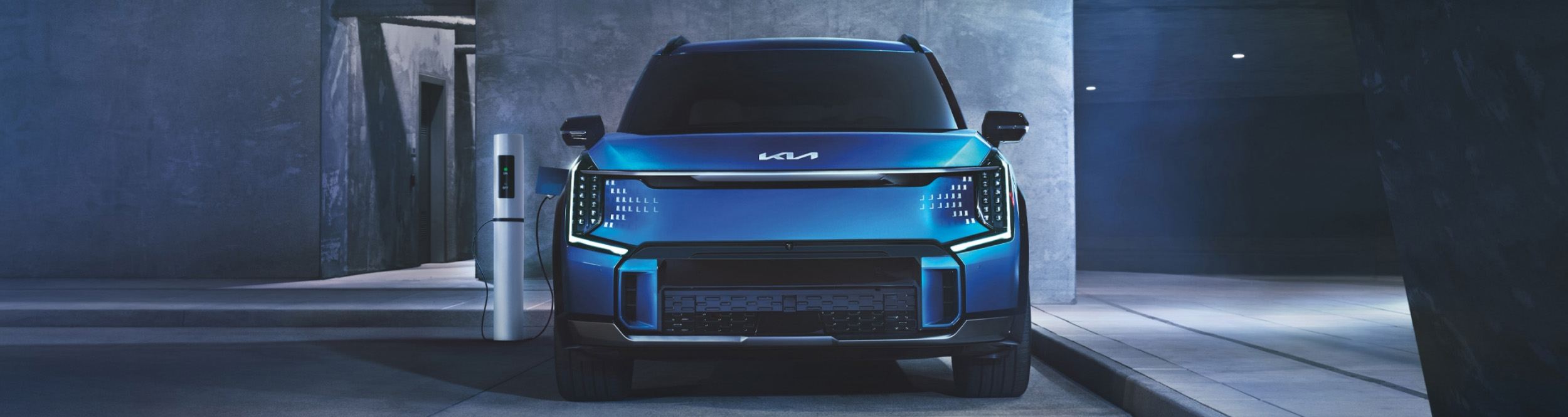 2024 Kia EV9 in blue, being charged while the owner is away in a modern building, front view