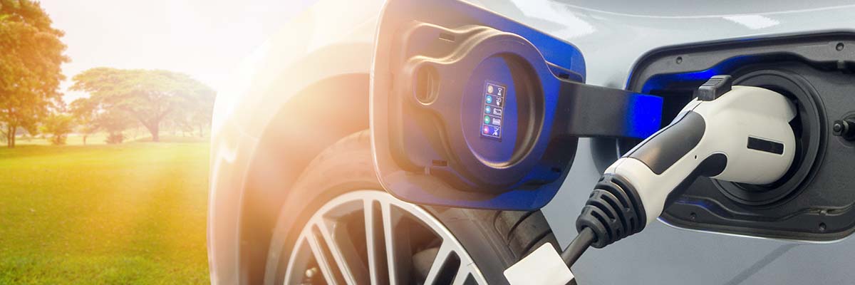 EV Car at charging station with the power cable supply plugged in on blurred nature with soft light background