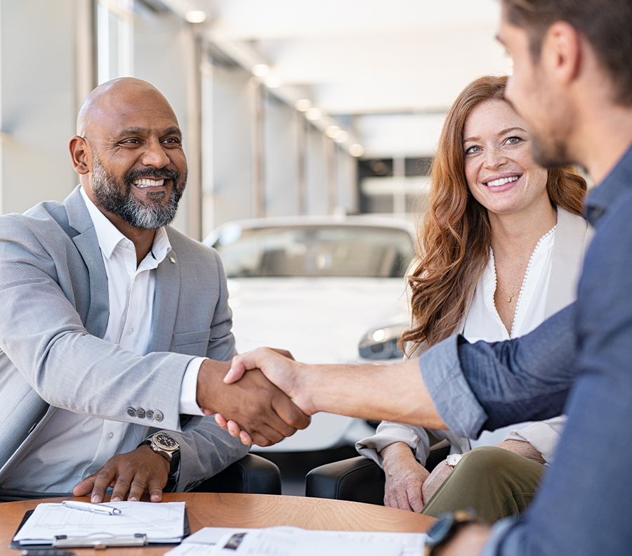 Dealership employee smiling shaking hands with satisfied customer.