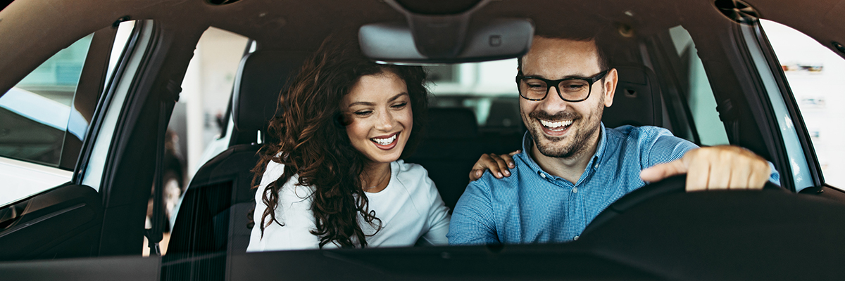 Happy couple enjoying while choosing and buying new car at showroom.