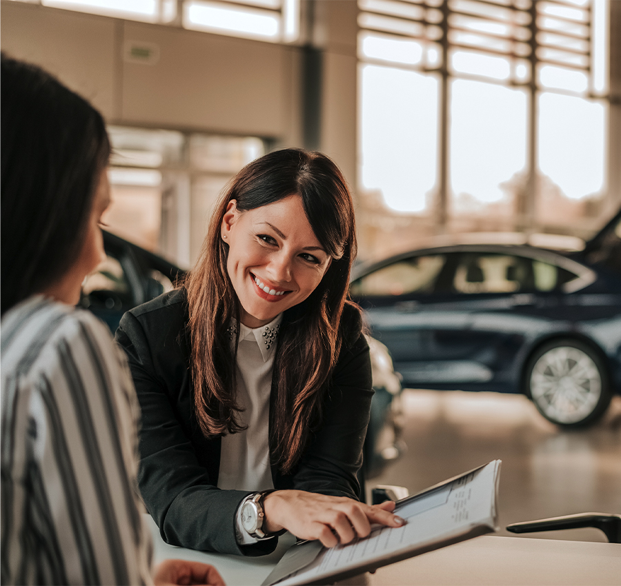 Smiling car saleswoman discussing a contract with a female customer.