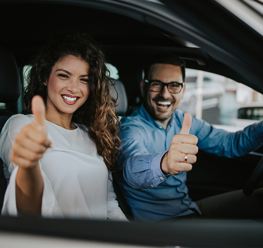 Happy middle age couple enjoying while choosing and buying new car at showroom.