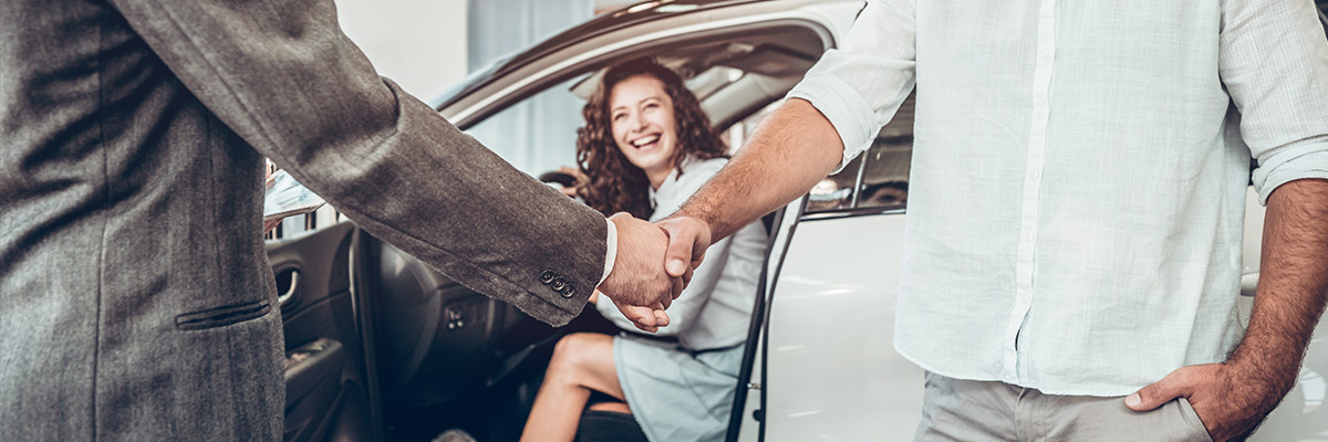 close up view of handshake of salesmen with the man in the showroom on the background of a woman in a new car