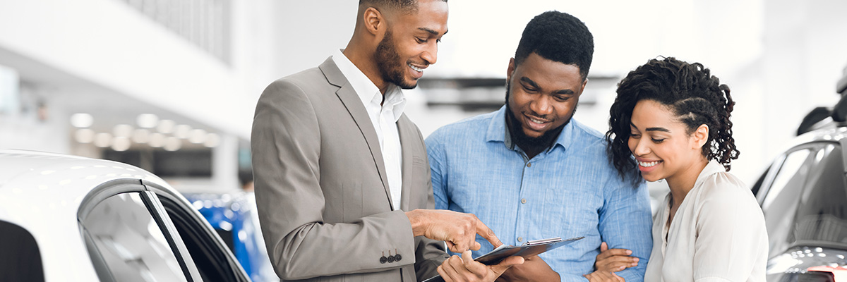 Customers speaking with a sales person at a car dealership