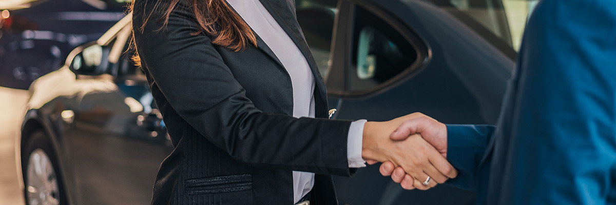 close up view of handshake of salesmen with the man in the showroom on the background of a woman in a new car
