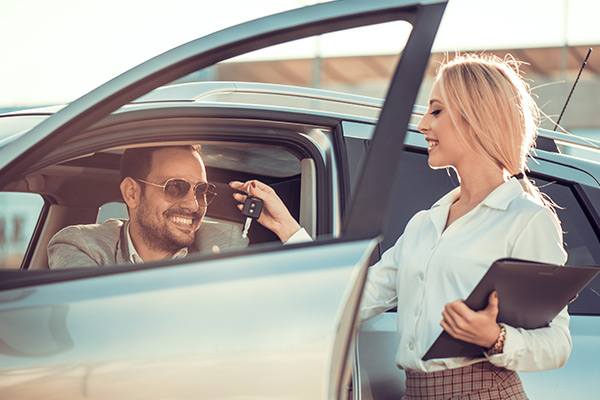 Dealership employee smiling handing keys to happy customer in driver seat