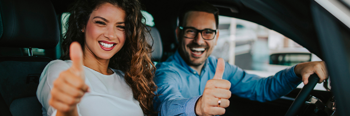 Close up of couple giving thumbs up and smiling in new car.