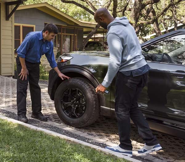Two men looking at the driver’s side front tire of a Ford Explorer