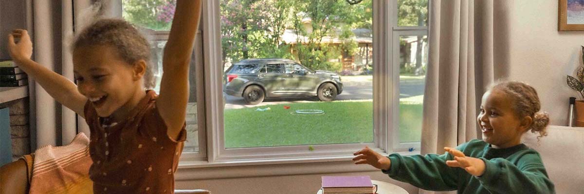 Two kids playing by a window with a Ford SUV parked outside