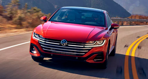 Front view of the Arteon in Kings Red Metallic driving on two-lane highway with mountains in background.