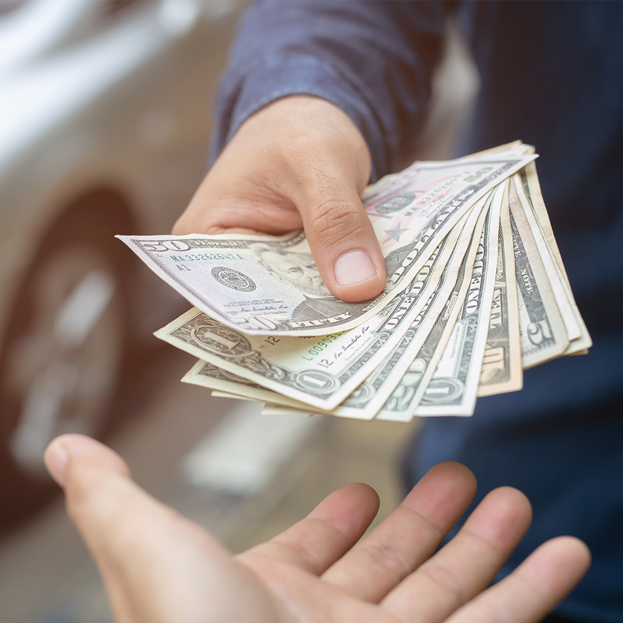 close up of a person handing over money to the dealership employee