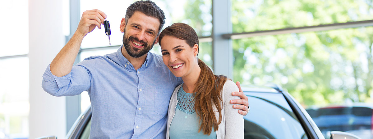 Couple smiling holding car keys in front of car in dealership