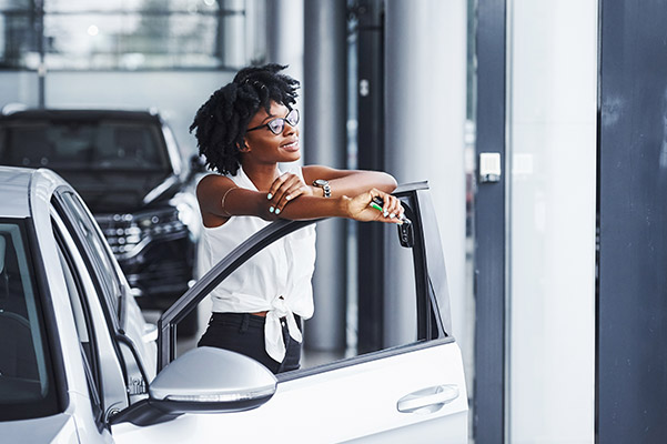 Woman looking outside resting on car door in dealership smiling.