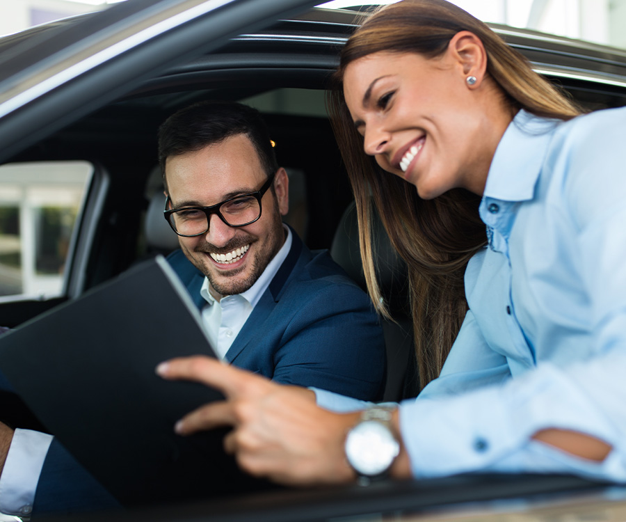 Saleswoman at the dealership showroom talking with customer and helping him to choose a new car for himself.