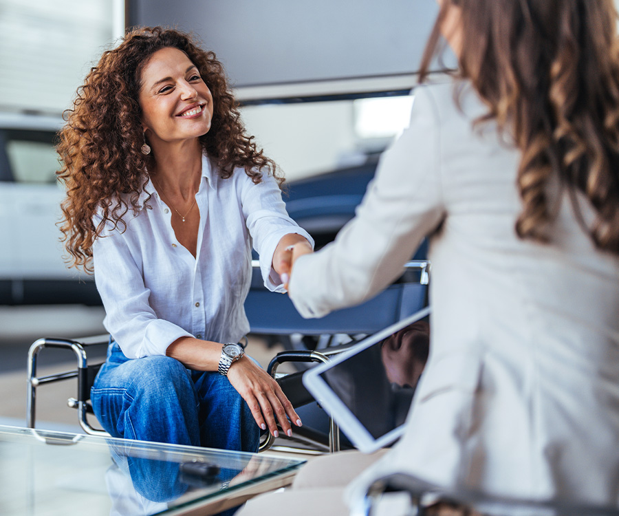 Happy woman buying a car and closing the deal with a handshake with the saleswoman at the dealership. Smiling car saleswoman discussing a contract with a female customer.