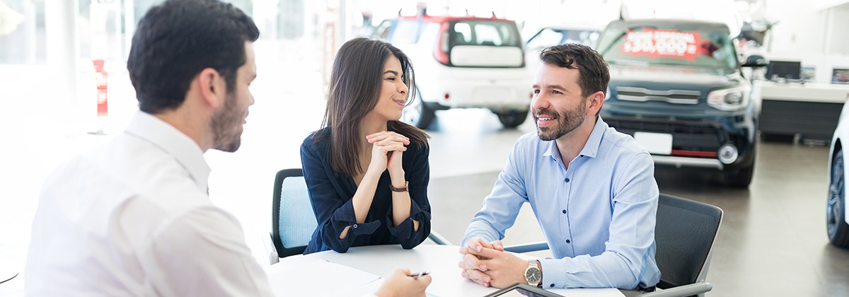 two people talking with a salesperson at a car dealership