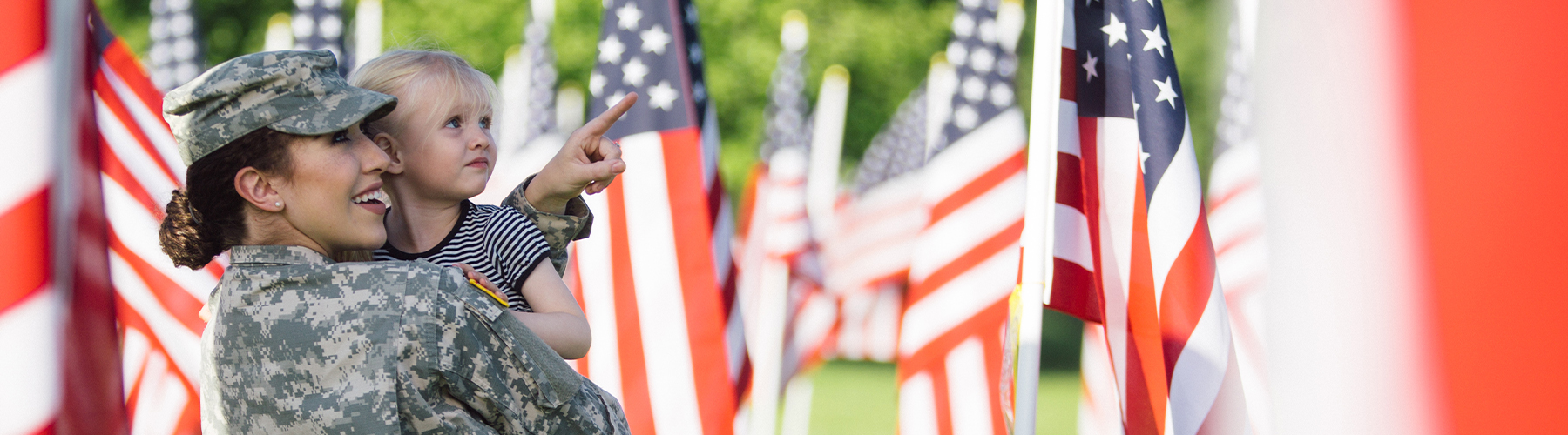 Soldier holding daughter looking at flags