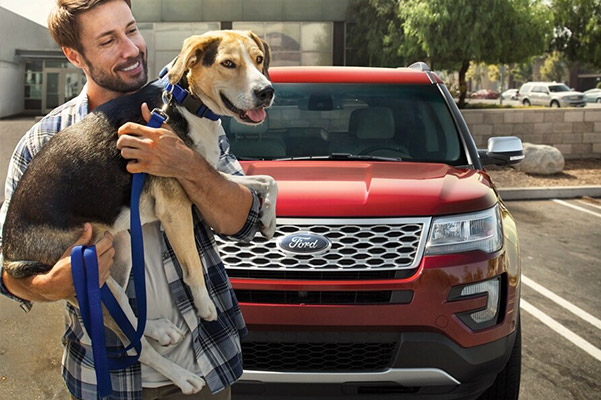 Man holding dog while standing infront of Ford Explorer