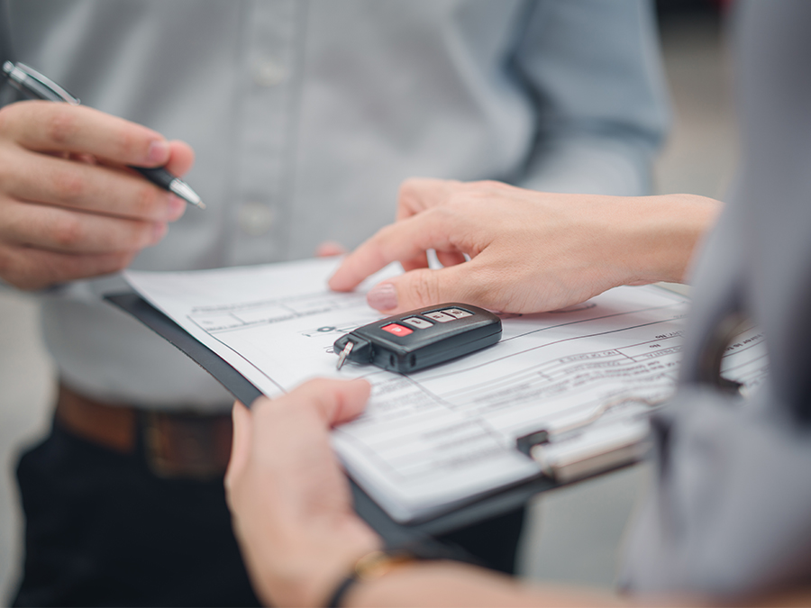 Dealership employee handing a clipboard to the customer with keys on it