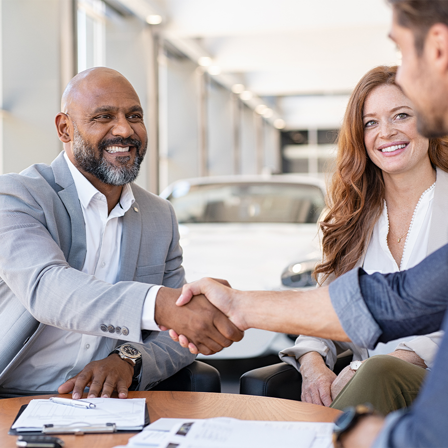 Dealership employee smiling shaking hands with satisfied customer.