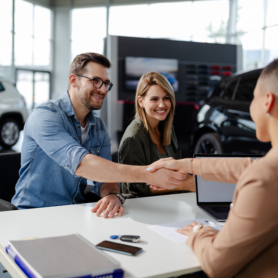 Dealership employee smiling shaking hands with satisfied customer.