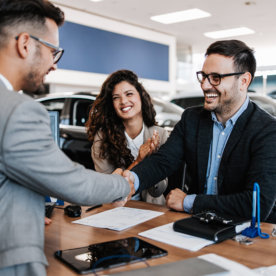 Dealership employee smiling shaking hands with satisfied customer.